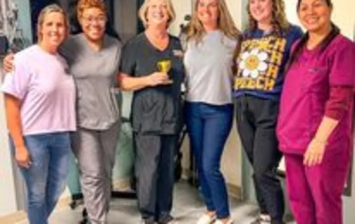 A group of people smiling and standing indoors in casual clothing.