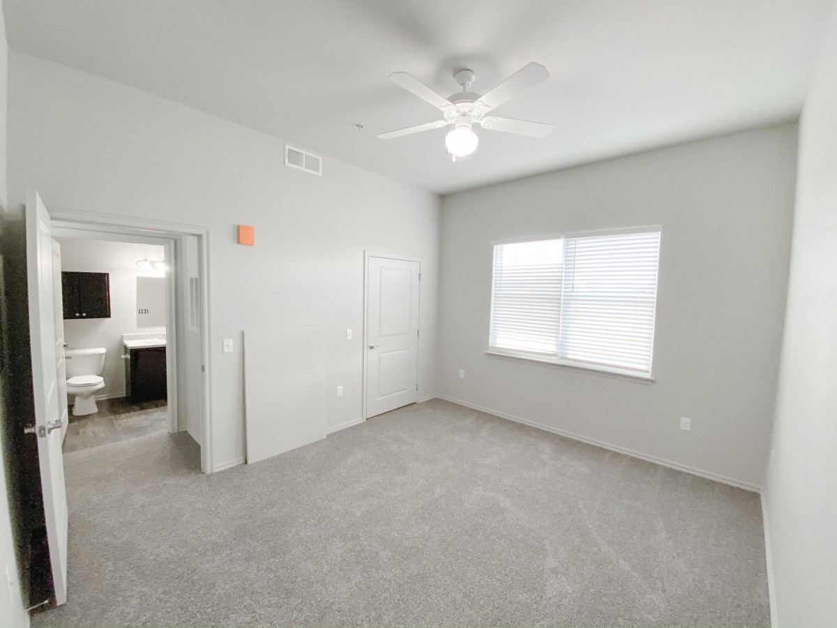 A bright, empty bedroom with a ceiling fan and carpet flooring.