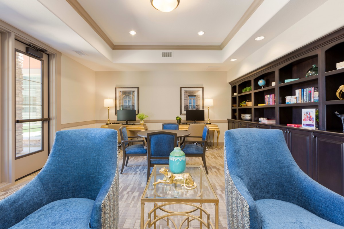 A cozy living room featuring blue armchairs, a decorative coffee table, and bookshelves along the wall.
