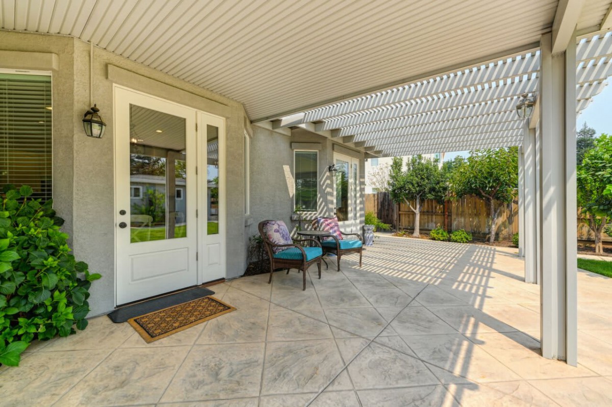 A cozy backyard patio with a pergola, featuring comfortable chairs and a small table against a garden backdrop.