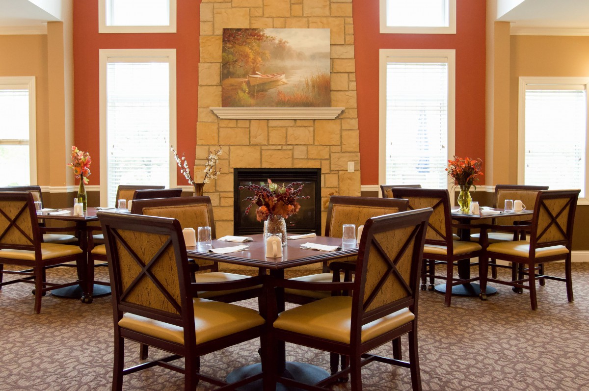 A cozy dining room with a warm fireplace, neatly set tables, and elegant artwork on the wall.
