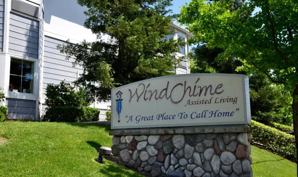 Sign for WindChime Assisted Living with a building and lush greenery in the background.