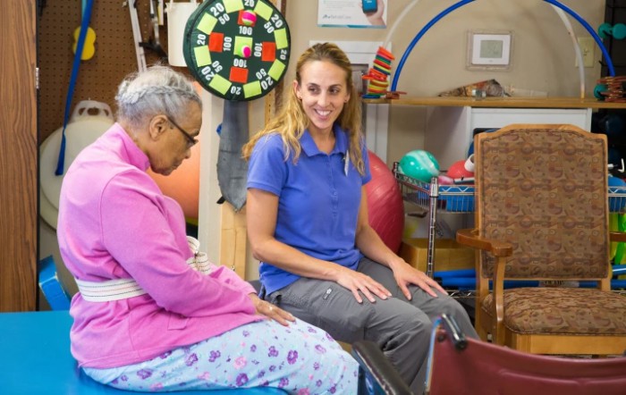 A therapist assists an elderly woman during a rehabilitation session in a healthcare setting.