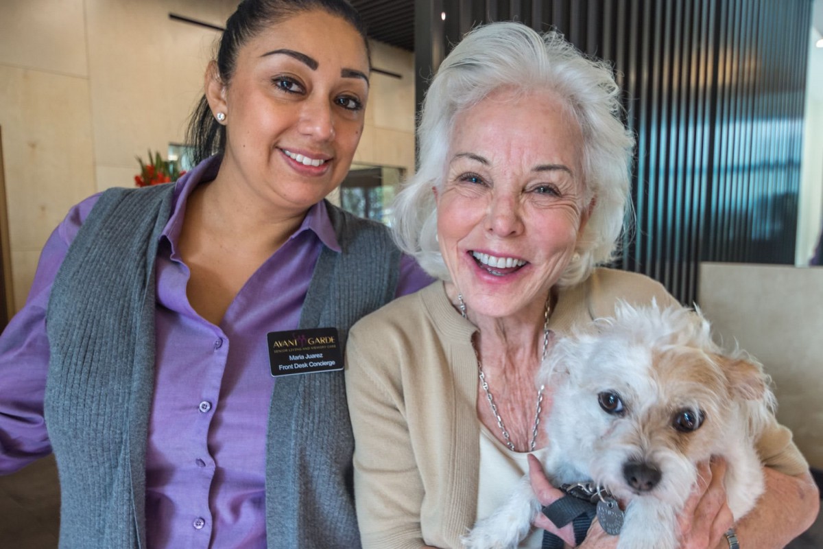 Two women smiling indoors, one holding a small dog.