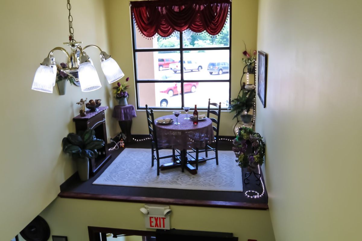 A cozy dining area with a table and two chairs by a large window, decorated with plants and elegant lighting.