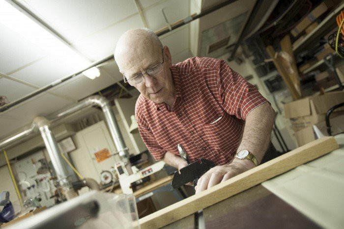 An elderly man diligently working on a woodworking project in a workshop.