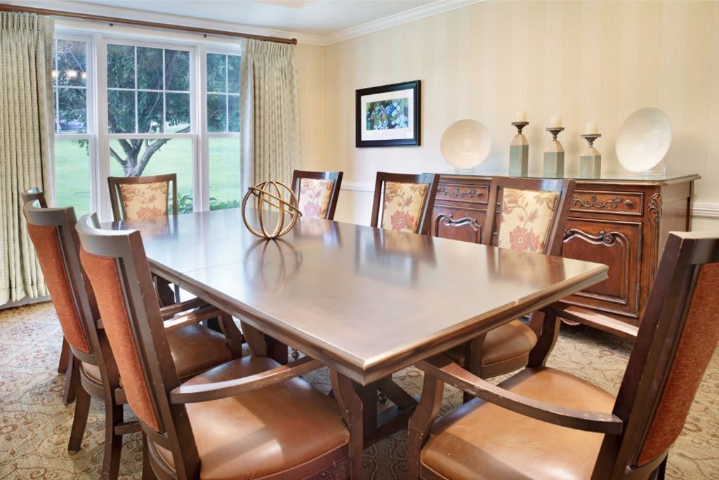 A spacious dining room with a large table and elegant chairs, complemented by tasteful decor and natural lighting from a window.
