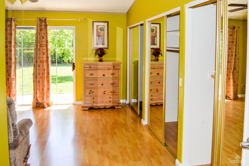 A bright bedroom with yellow walls, wood flooring, a dresser, and mirrored closet doors.