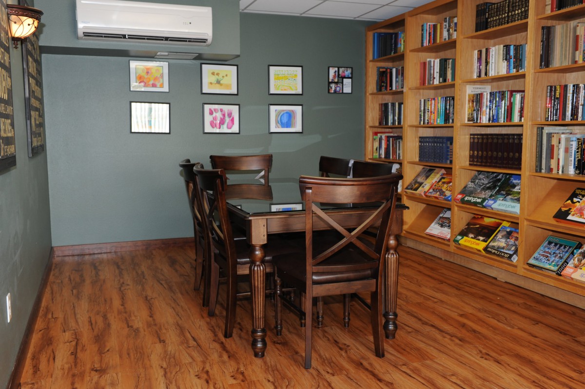 A cozy library room with a wooden table and chairs, surrounded by bookshelves and adorned with art on the walls.