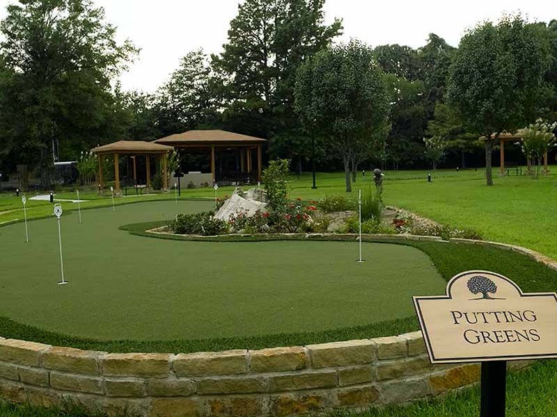 A beautifully landscaped putting green surrounded by trees and garden elements.