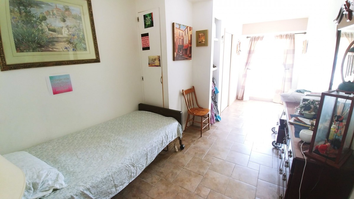 A simple bedroom with a single bed, artwork on the walls, and abundant natural light.
