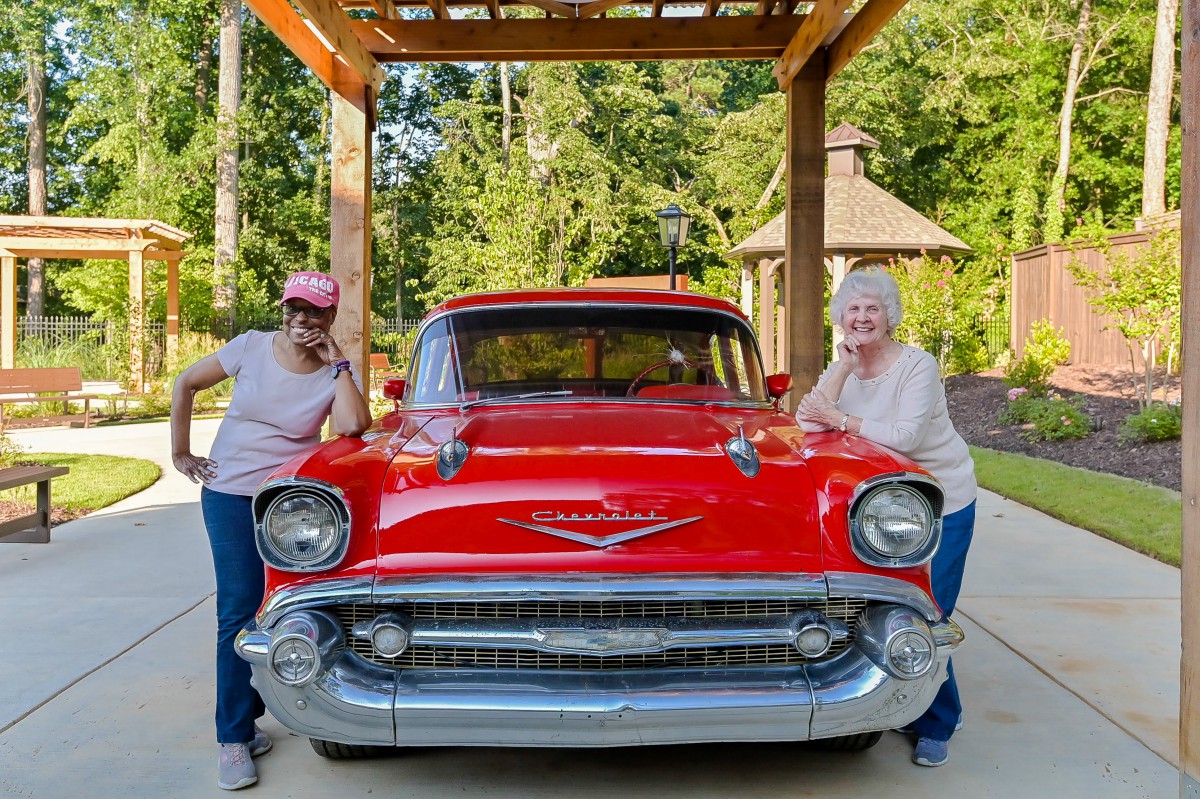 Two people smiling and posing with a red vintage Chevrolet in an outdoor setting.