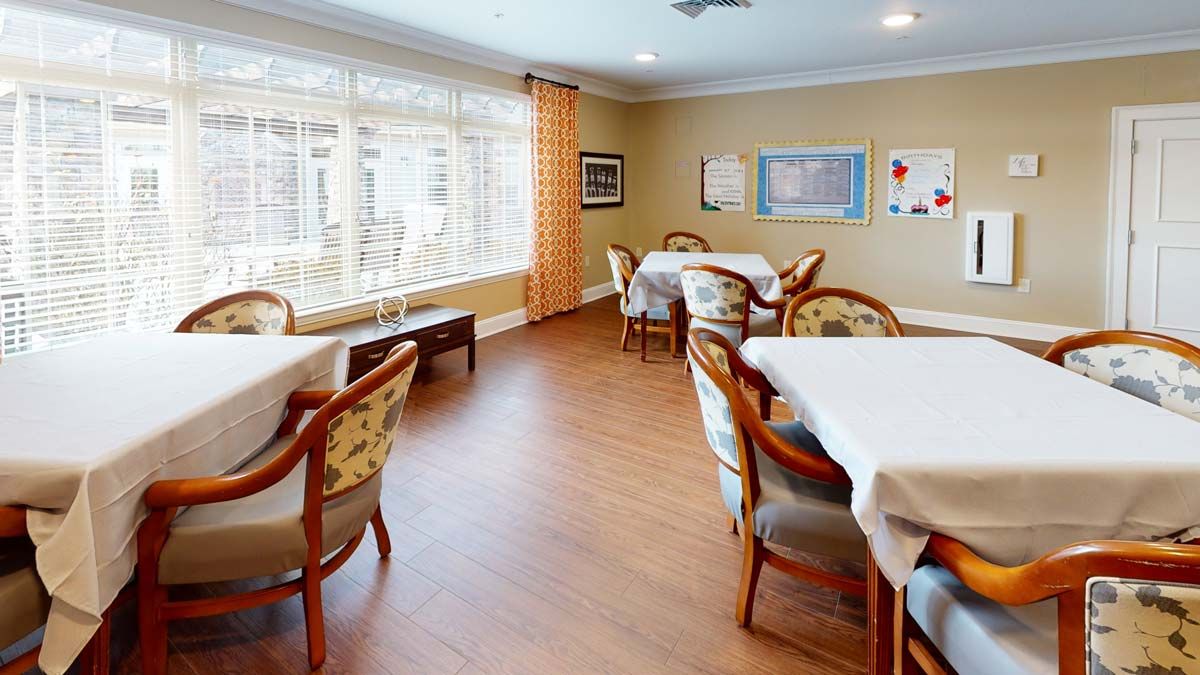 A cozy dining area with several tables and chairs, featuring large windows and wall decorations.