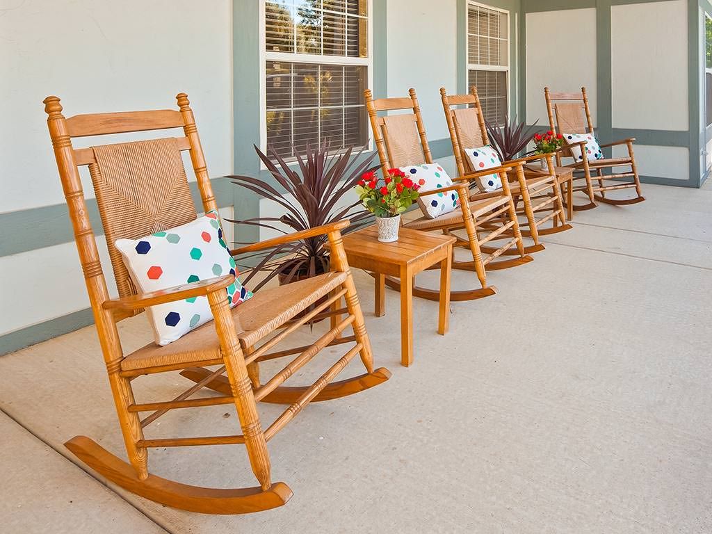 A row of wooden rocking chairs with colorful cushions on a porch.