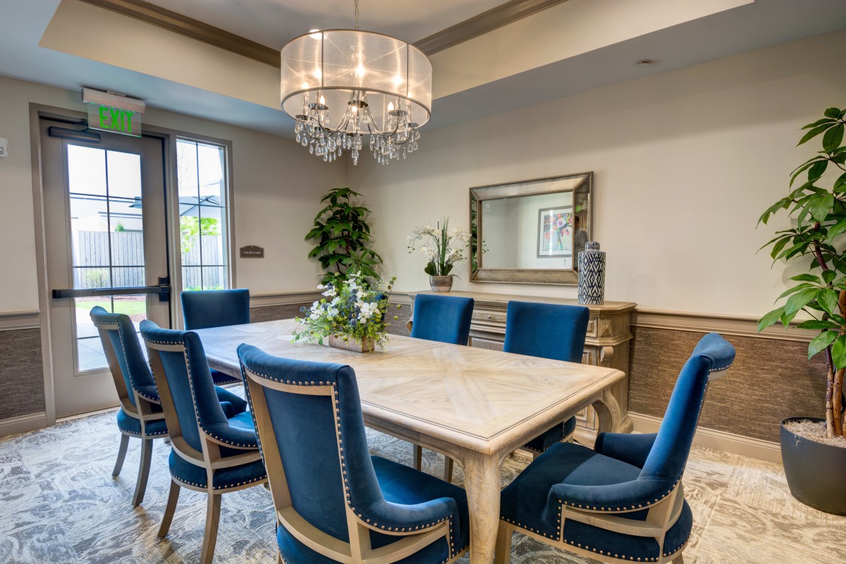 A luxurious dining room with a large table, blue upholstered chairs, and an elegant chandelier.