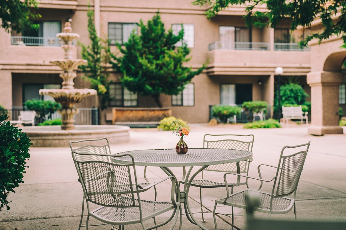 A peaceful outdoor patio with a table and chairs set near a fountain in an apartment complex.
