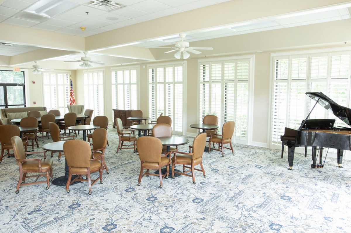 A bright and spacious interior dining area with multiple tables and chairs, large windows, and a piano in the corner.