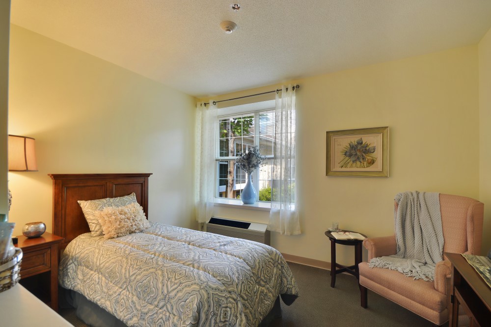 A cozy bedroom with a single bed, armchair, and a window letting in natural light.