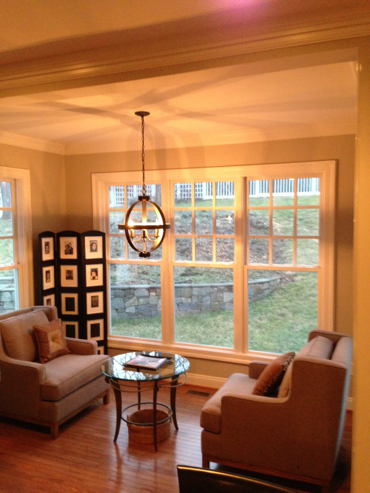 A cozy living room with ample natural light, featuring two chairs and a small table by large windows.