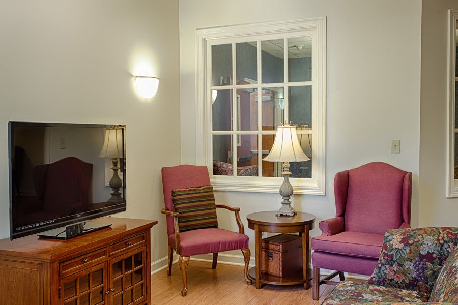 A cozy living room with two chairs, a lamp on a side table, and a television.