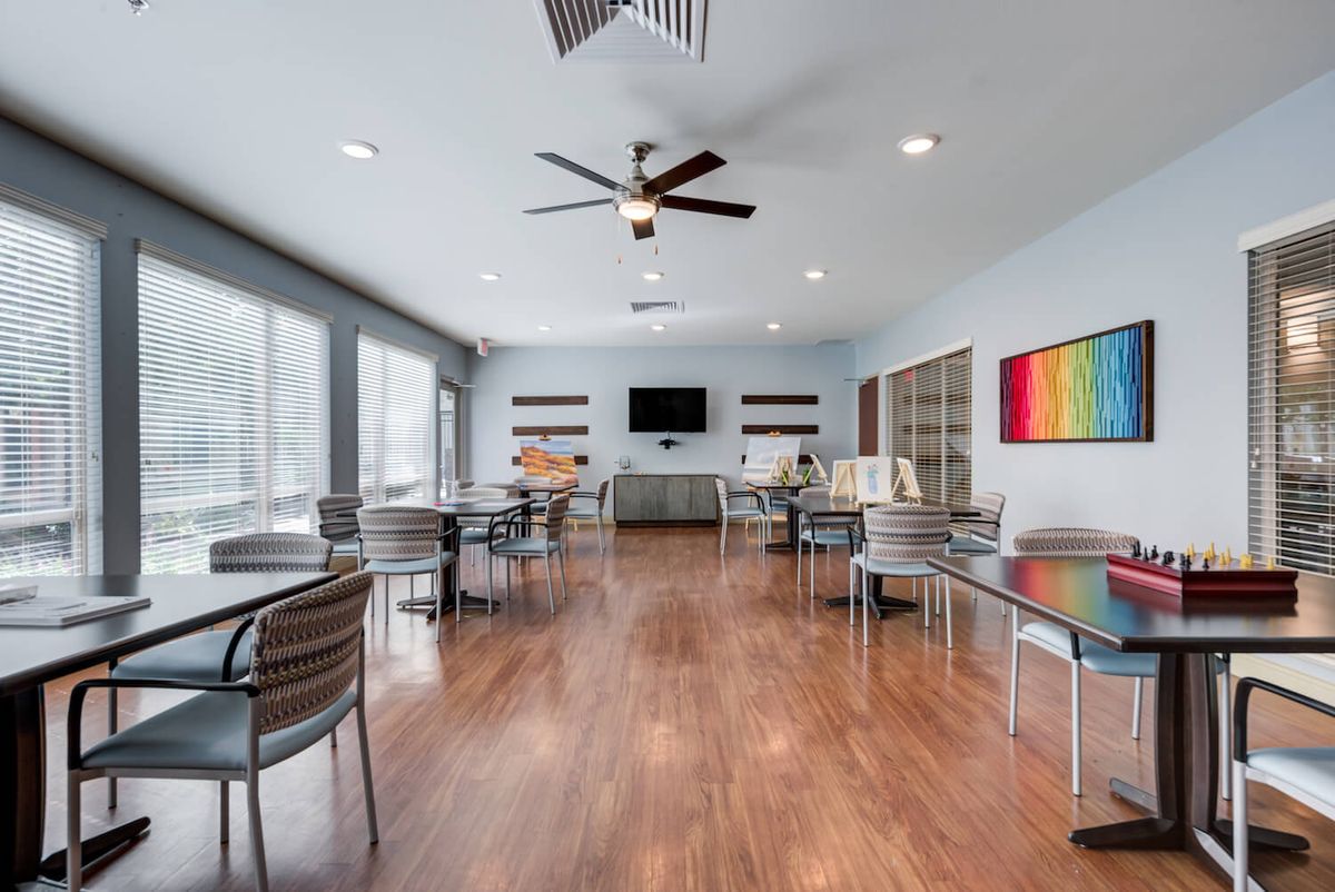 A modern conference room with wooden floors, multiple tables and chairs, a television, and artwork on the wall.