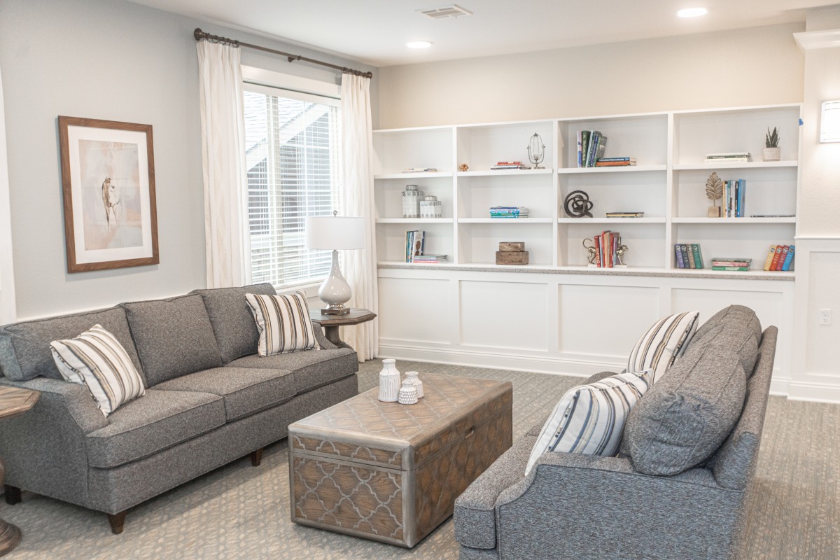 A modern living room with neutral tones featuring two gray sofas, a central table, and a large white bookshelf.