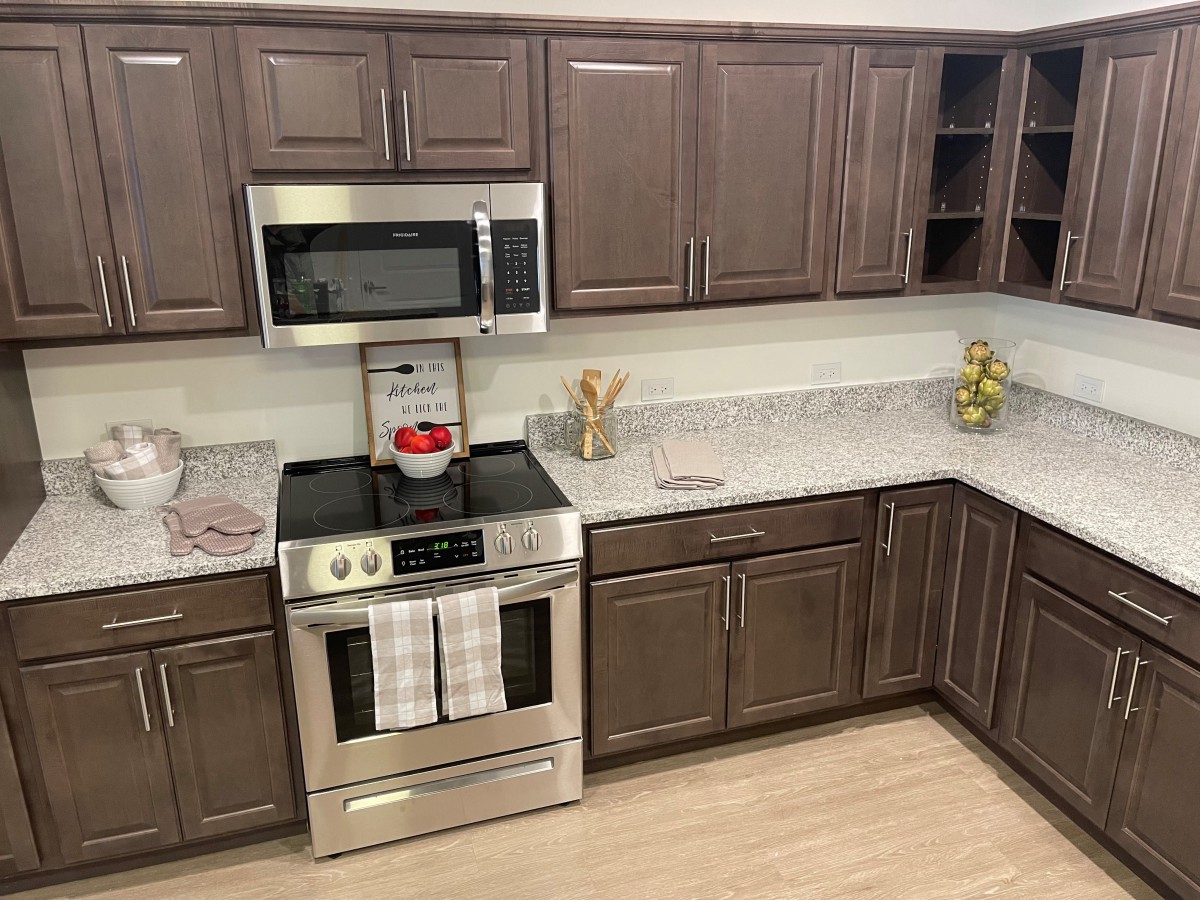 A modern kitchen with brown cabinets, stainless steel appliances, and a neatly organized countertop.