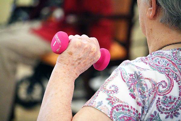 A senior person exercising with a pink dumbbell.