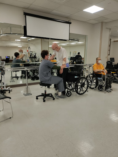 A therapy session in a rehabilitation center with patients using wheelchairs and healthcare professionals assisting.