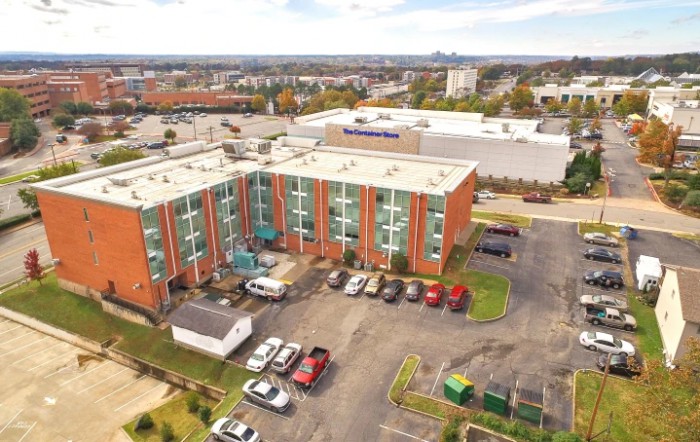 An aerial view of a mid-sized apartment building with a parking lot and surrounding cityscape.