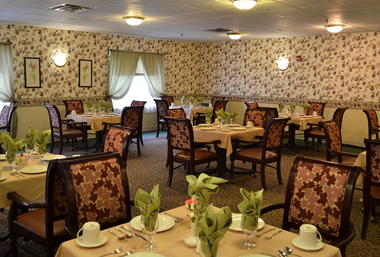 A cozy dining room with elegantly set tables and floral wallpaper.