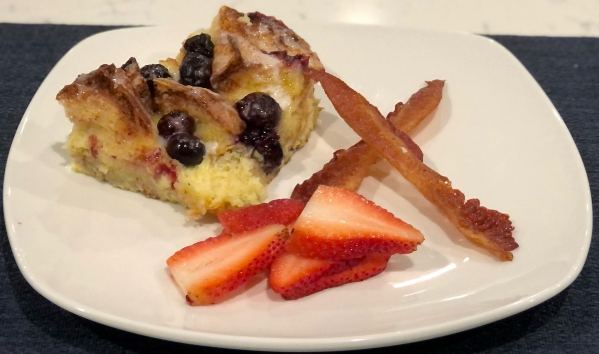 A slice of berry-topped cake served with fresh strawberries on a white plate.