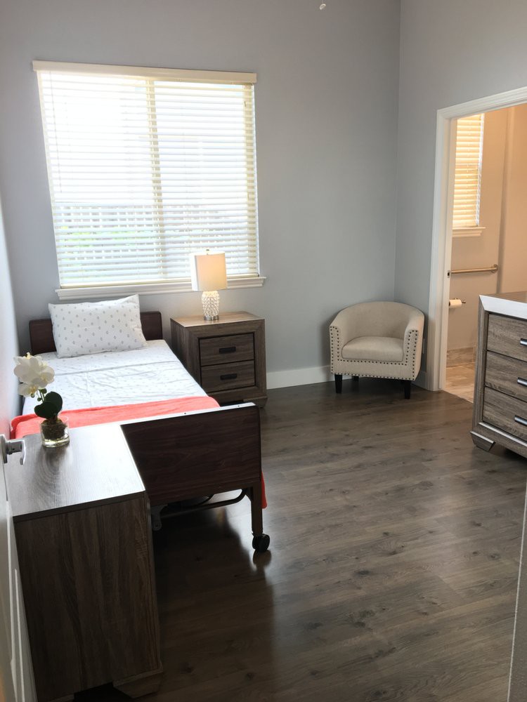 A minimalist bedroom with a single bed, dresser, and chair complemented by a large window.