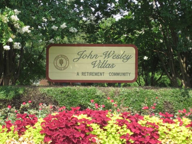A sign for John Wesley Villas, a retirement community, surrounded by a landscaped garden with colorful flowers.