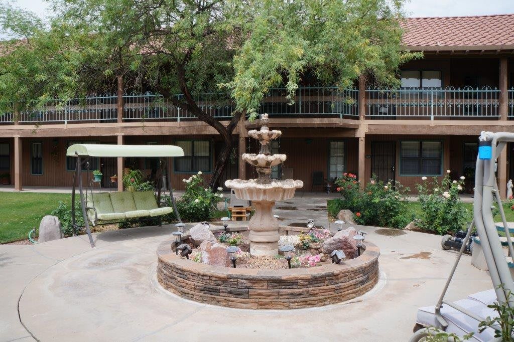 A serene courtyard featuring a tiered fountain surrounded by greenery and a swing.