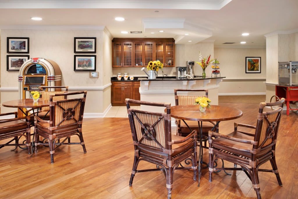 A cozy dining area featuring wooden tables and chairs with a view of a modern kitchen in the background.