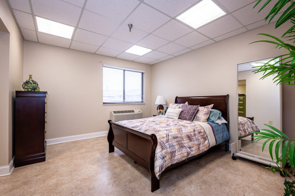 A cozy bedroom with a wooden bed, decorative pillows, a mirror, and natural light coming through the window.