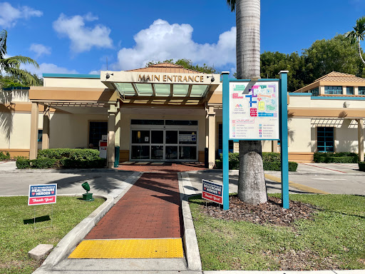 Main entrance of a public building with informational signage and palm trees.