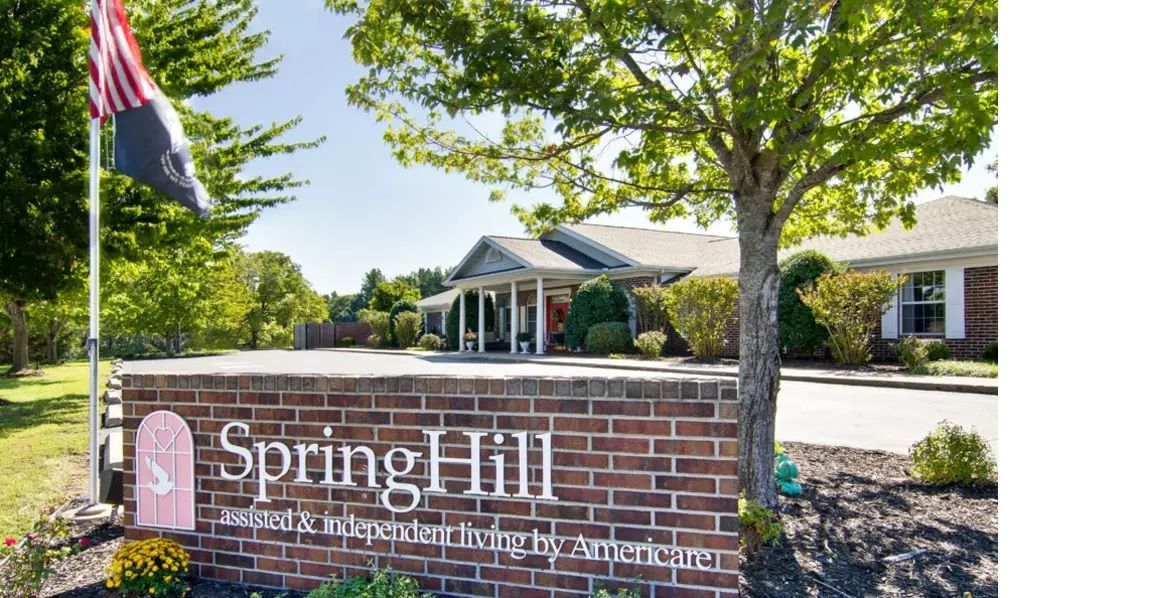 A view of a building with a prominent brick sign, tree, and well-maintained landscaping.