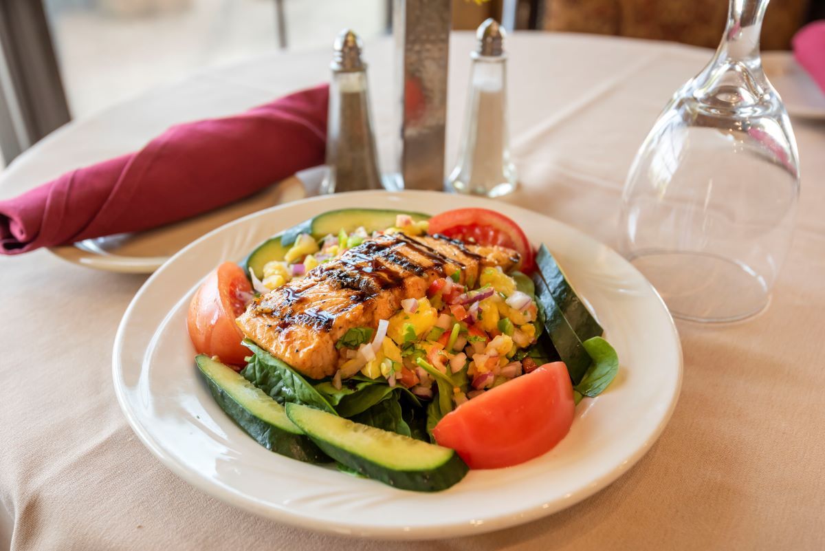 A plate of grilled salmon served on a bed of fresh salad with cucumbers and tomatoes in a restaurant setting.