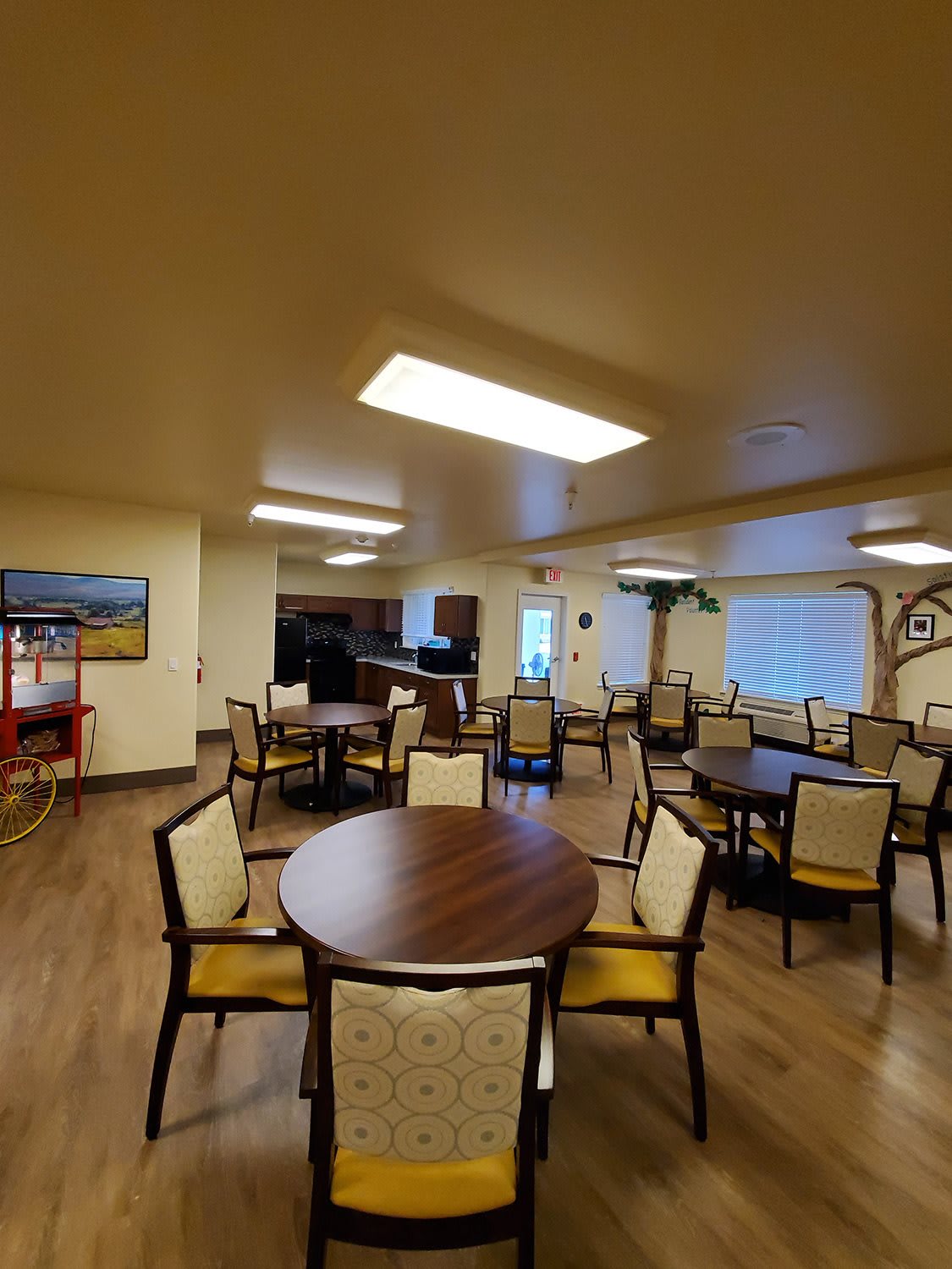 A spacious dining room with multiple tables and chairs, featuring wood flooring and ample lighting.