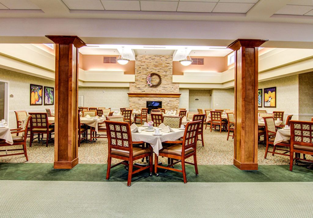 A well-lit dining area with neatly arranged tables and chairs, featuring a stone fireplace as the focal point.