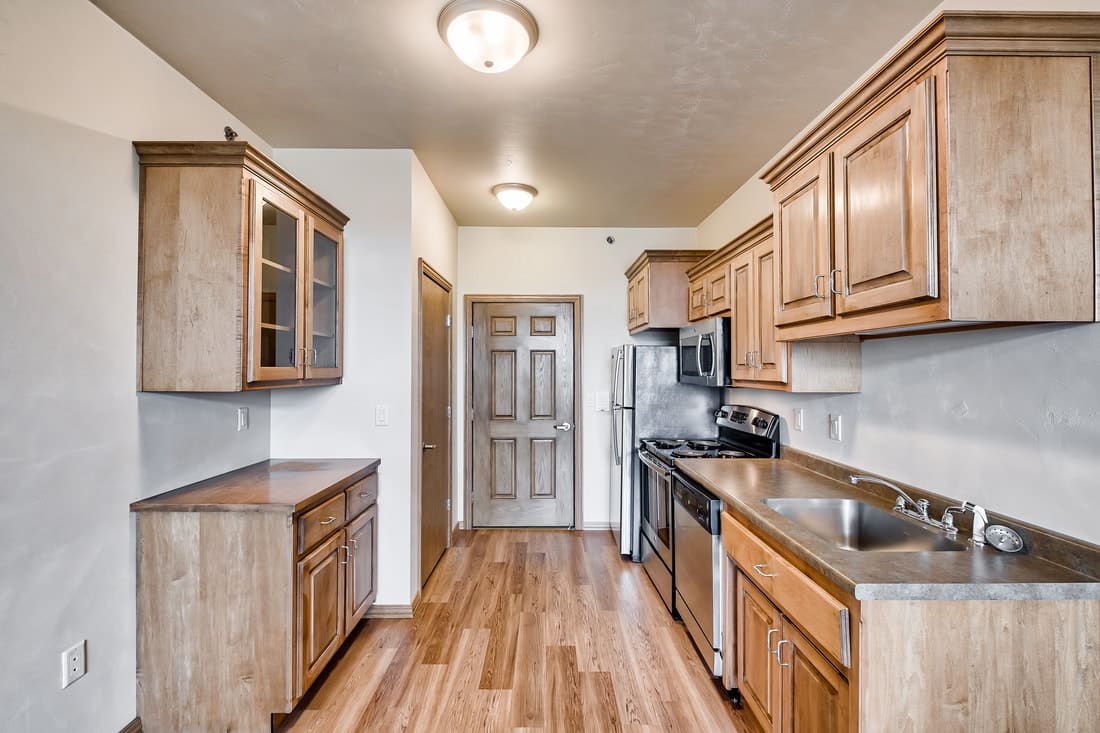 A modern kitchen with wooden cabinets, stainless steel appliances, and a hardwood floor.