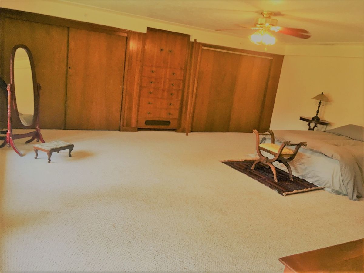 A spacious room with wooden paneling, modest furniture, and a ceiling fan.