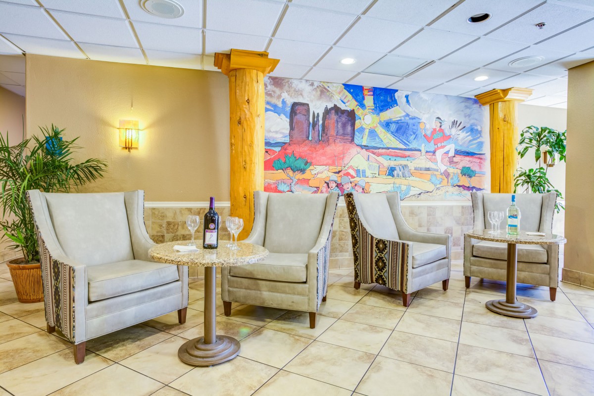 A cozy lobby seating area with chairs, a table holding a wine bottle, and colorful wall art.