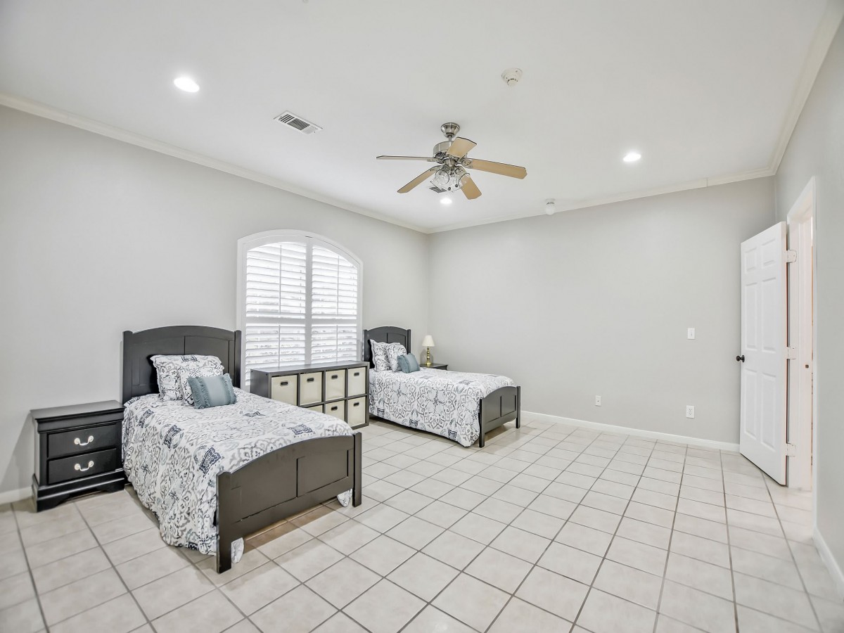 A spacious bedroom with twin beds, tiled flooring, and a ceiling fan.