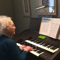An elderly woman playing the organ indoors with sheet music.
