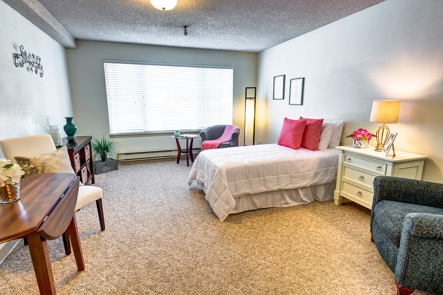 A cozy bedroom featuring a single bed, comfortable chairs, and large window.
