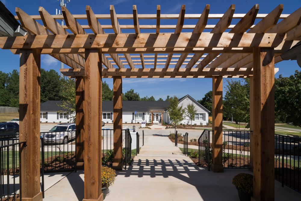A wooden pergola casts shadows over a walkway leading to residential buildings.
