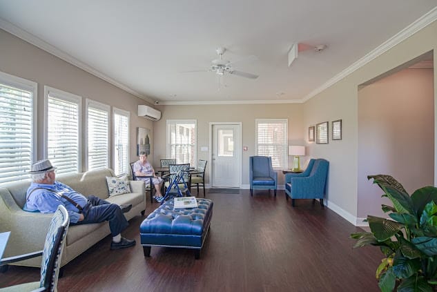 A spacious living room with comfortable seating, large windows, and a ceiling fan.